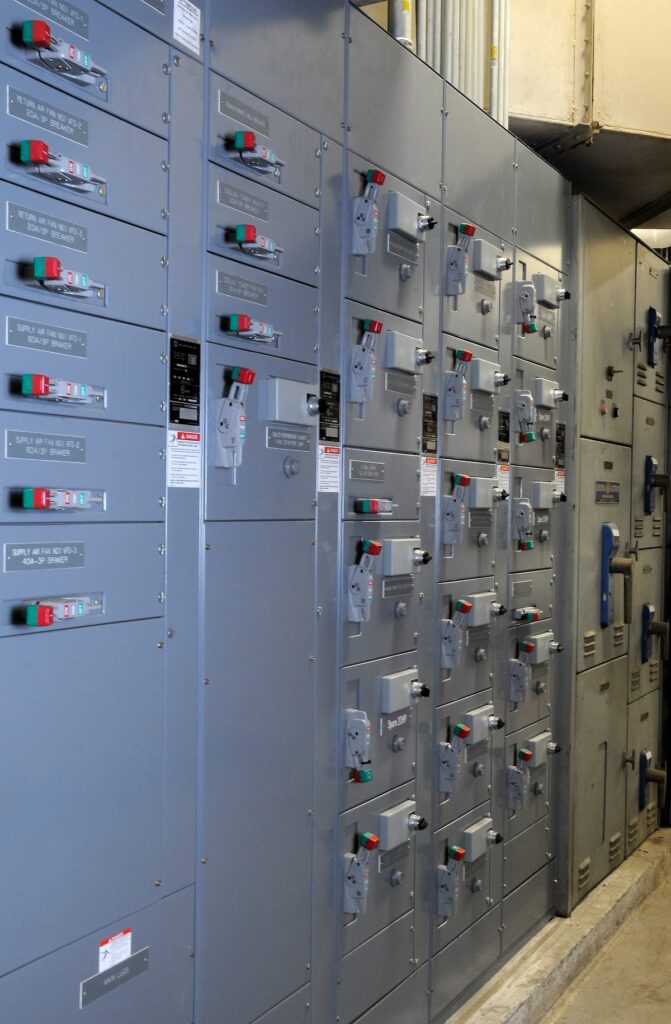 A series of gray electrical switchgear panels lined up in an industrial environment, each featuring various switches, handles, and indicator lights.