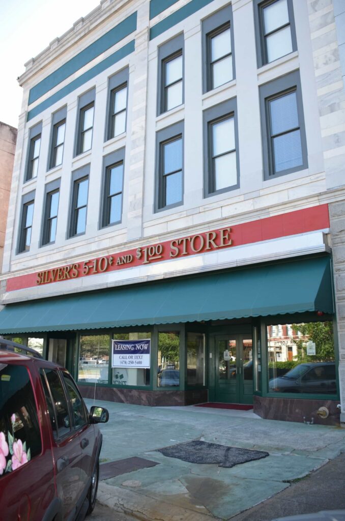 A building with a sign reading SILVER’S 5-10¢ AND $1.00 STORE. The entrance has green trim and awnings, and a LEASING NOW sign is posted in the window. A red vehicle is parked in front.