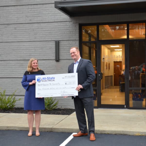 A smiling woman and man stand outdoors, holding a large $10,000 All-State Electrical check dated 10/21/2020.