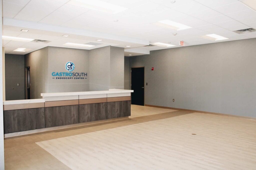 Modern medical office lobby with gray walls, white ceiling, wood-accented reception desk, and GastroSouth Endoscopy Center logo on the wall. The space is clean, open, and brightly lit.