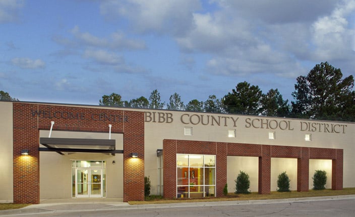 A brick and beige building with large windows and the words Bibb County School District on the front, set against a backdrop of trees and a cloudy sky.