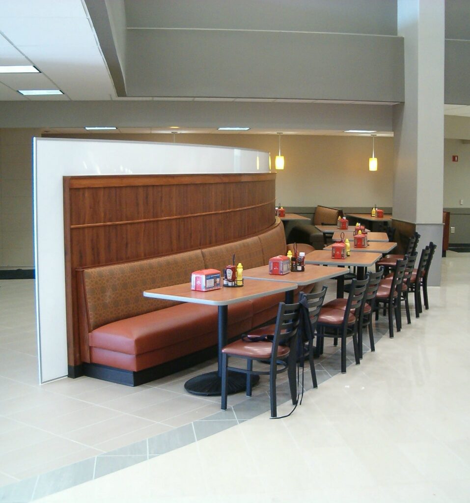 A row of vacant restaurant booths and tables with chairs, featuring red condiment bottles and napkin holders in a brightly lit, contemporary dining space.