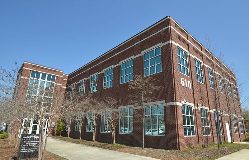 A two-story red brick building featuring numerous windows and the number 610 displayed on its side, set beneath a clear blue sky with leafless trees and a sidewalk in front.