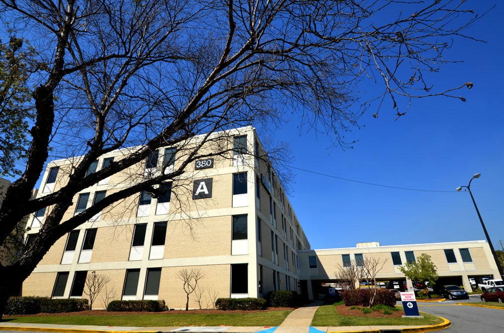 A beige office building with a sign reading 350 A, leafless trees in front, clear blue sky, and a sidewalk leading toward the entrance.