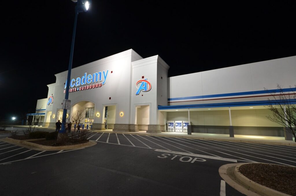 A large Academy Sports + Outdoors store at night, illuminated by exterior lighting, with an empty parking lot and a clearly visible entrance.