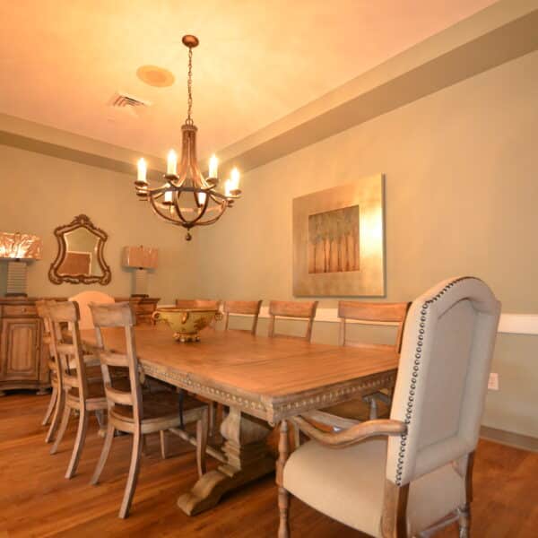 Spacious dining room featuring a wooden table surrounded by ten chairs, a chandelier overhead, sideboard, mirrors, and a framed painting on green walls, with a wooden floor and high ceiling.